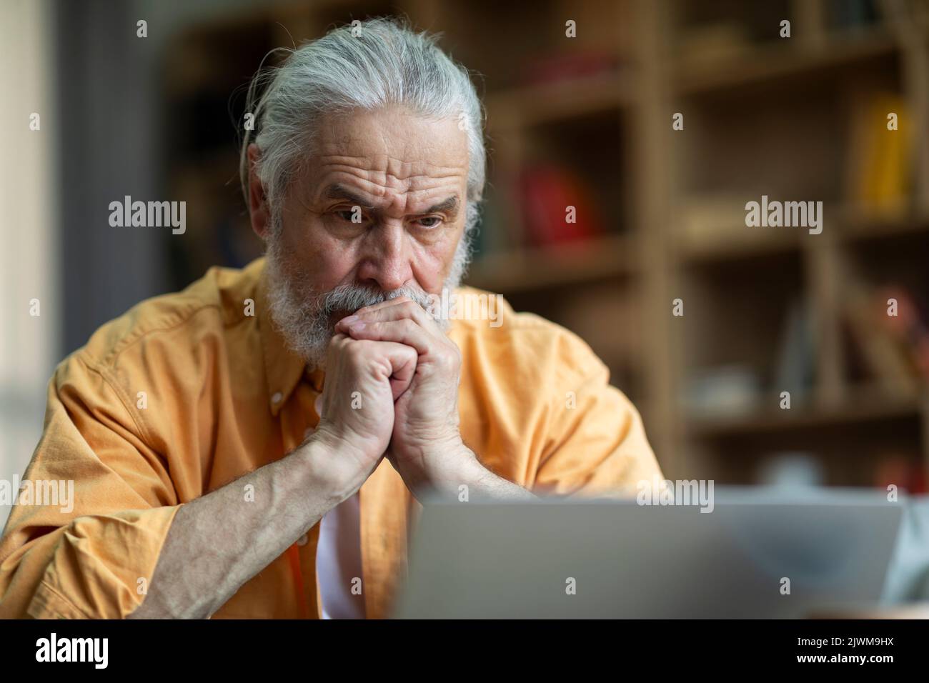 Pensionato concentrato seduto di fronte al notebook a casa Foto Stock