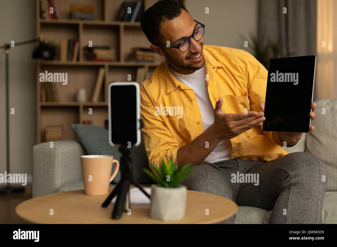 Allegro giovane nero maschio blogger registrazione video recensione di nuovo tablet digitale sul cellulare a casa, mockup Foto Stock