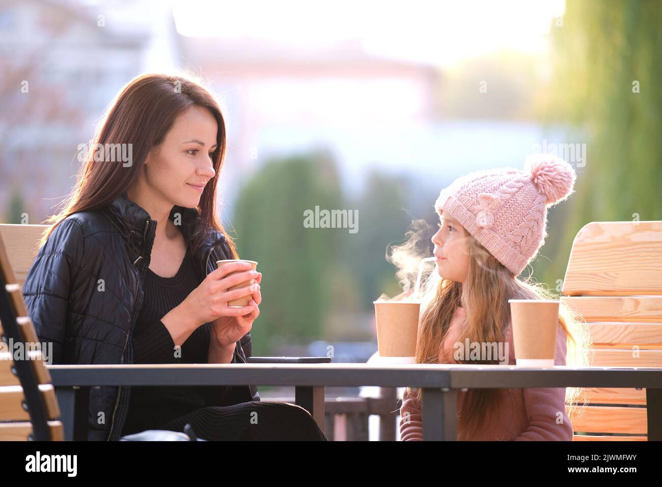 La giovane madre e la figlia del bambino hanno buon tempo insieme seduti al caffè di strada con bevande calde il giorno di autunno soleggiato. Felicità nelle relazioni familiari Foto Stock