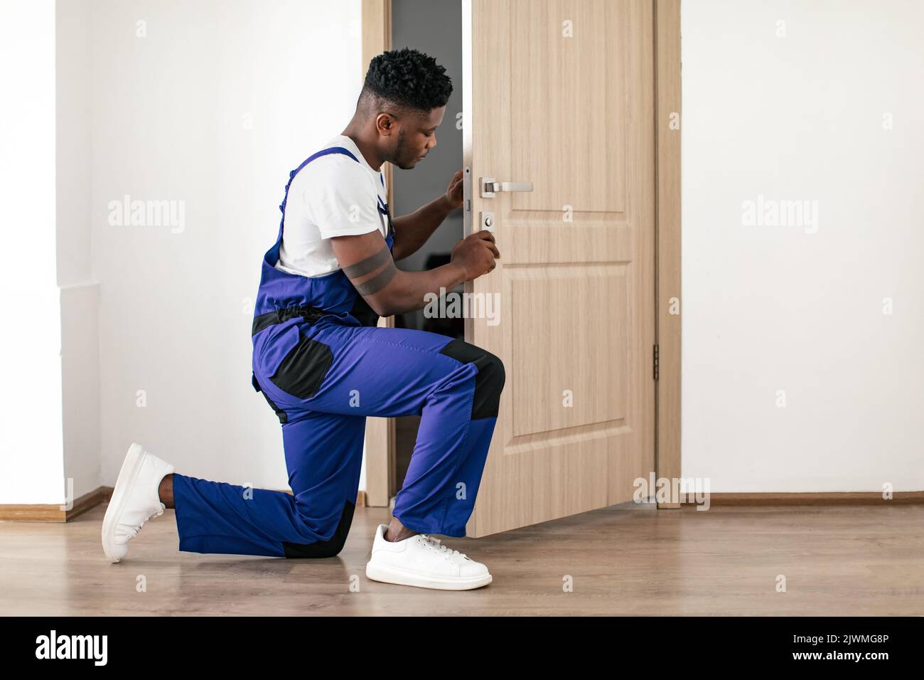 African American Male Worker Installazione di una nuova porta in Appartamento interno Foto Stock