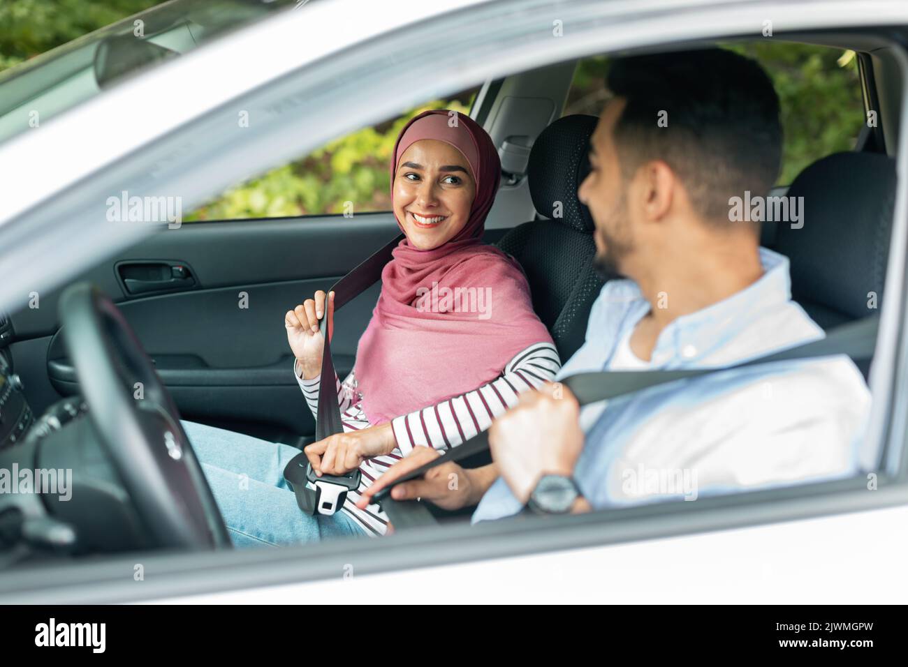 Sorridente millenario medio orientale signora in hijab e maschio allacciare le cinture di sicurezza, godere di viaggiare in auto Foto Stock