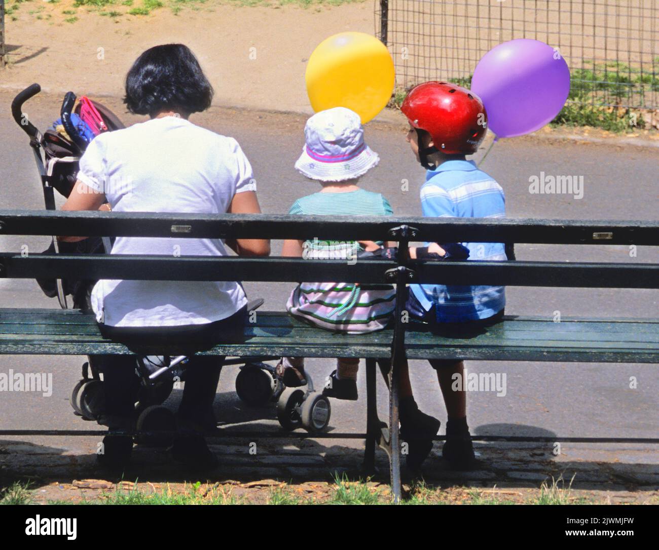 Bambinaia o madre e bambini a Central Park due bambini con palloncini seduti su una panchina nel parco giochi di New York. Vista posteriore. STATI UNITI Foto Stock