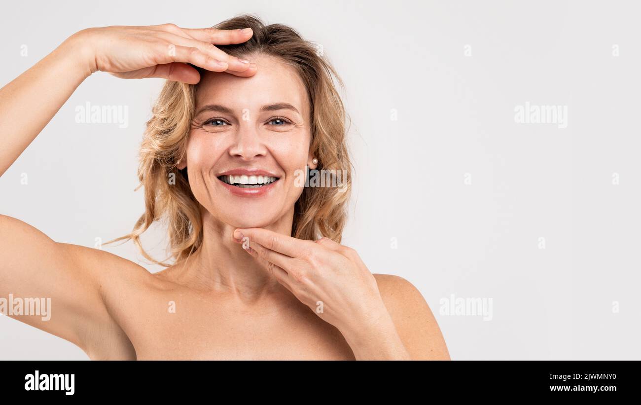 Concetto di Facebuilding. Felice bella donna di mezza età che tocca il mento e la fronte Foto Stock
