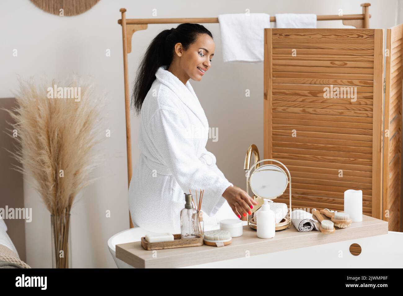 Donna nera con prodotti cosmetici seduta sulla vasca da bagno Foto Stock