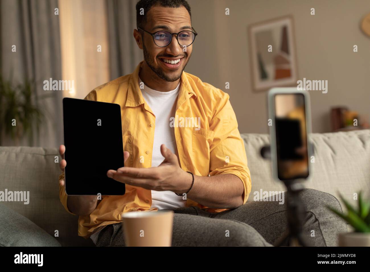 Positivo giovane nero maschio blogger registrazione video recensione di nuovo computer tablet sul cellulare a casa, mockup Foto Stock