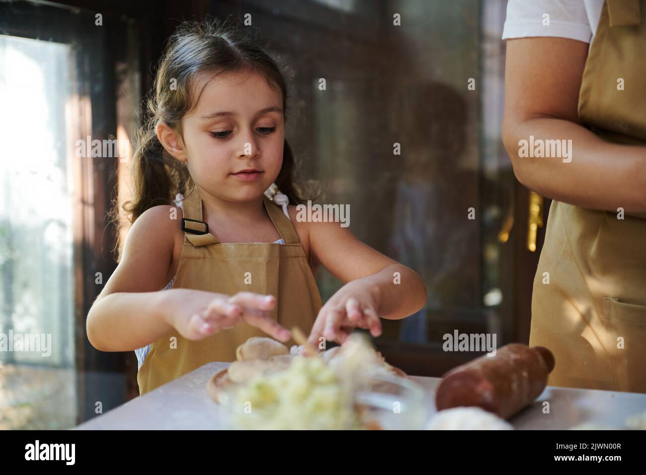 Adorabile bambina che indossa il grembiule dello chef, gnocchi ripieni di purè di patate, aiutando la mamma in cucina Foto Stock