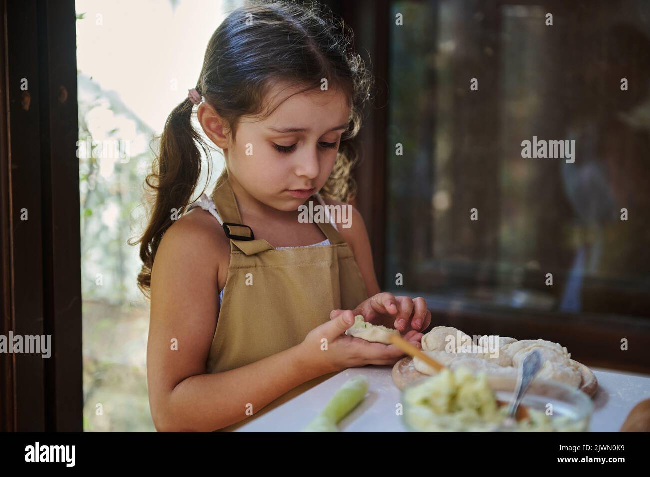Bella cuoca, adorabile bambina con due ponytail, nel grembiule dello chef purè di patate e formine gnocchi Foto Stock