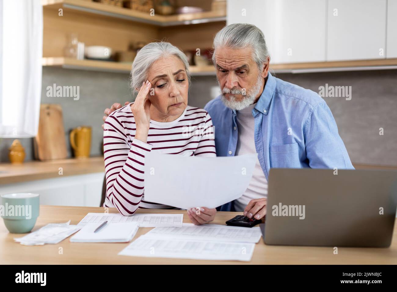Gli sposi anziani di rovesciamento che leggono i documenti mentre calcolano il preventivo della famiglia in cucina Foto Stock