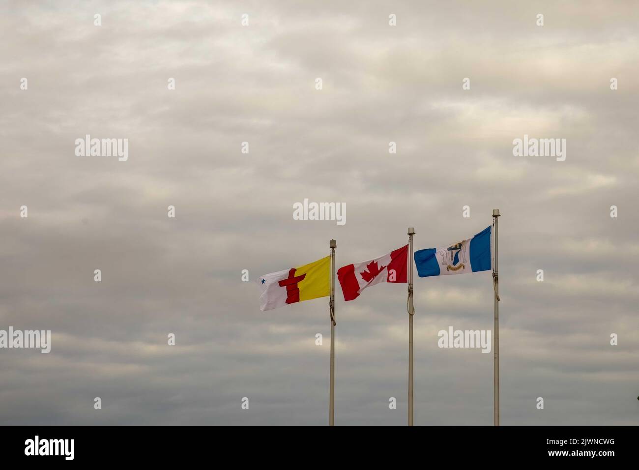 Bandiera del nuovo territorio Nunavut accanto alla bandiera canadese e alla bandiera del comune di Cambridge Bay a Cambridge Bay, Victoria Island, Nunavut, Canada contro gre Foto Stock