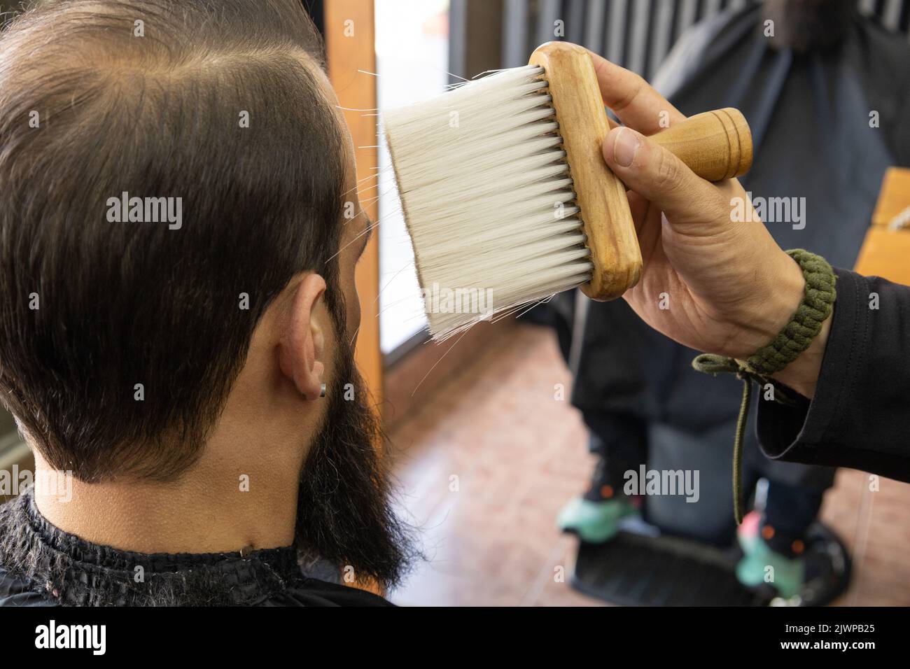 interno di un barbiere con un cliente con capelli corti e una barba seduta, servizio mentre uno stilista sta tenendo una spazzola, strumenti per la cura personale Foto Stock