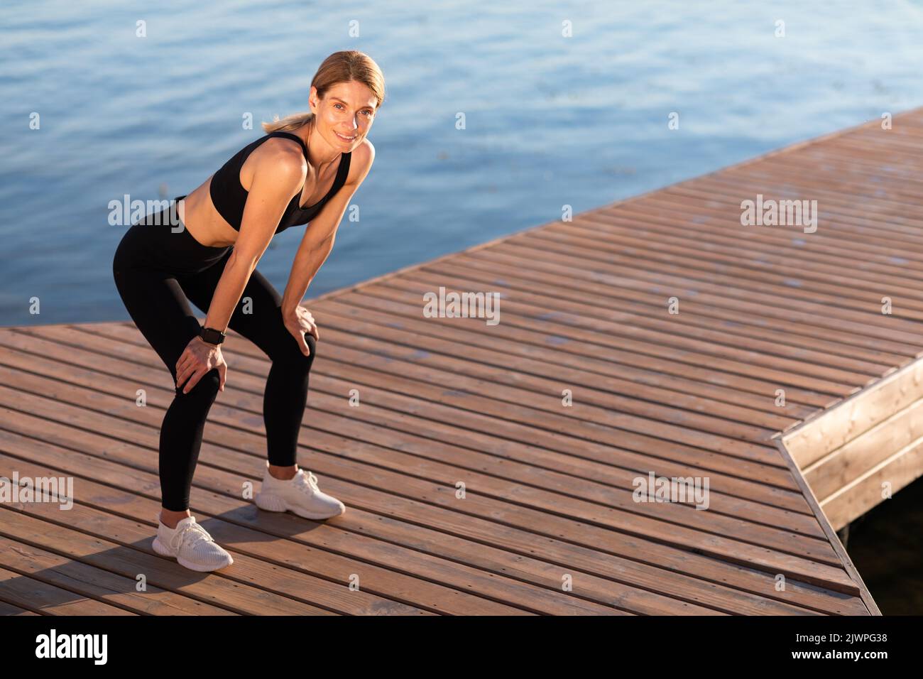 Donna sportiva che prende la rottura mentre si alleni all'aperto, appoggiando le mani sulle ginocchia Foto Stock