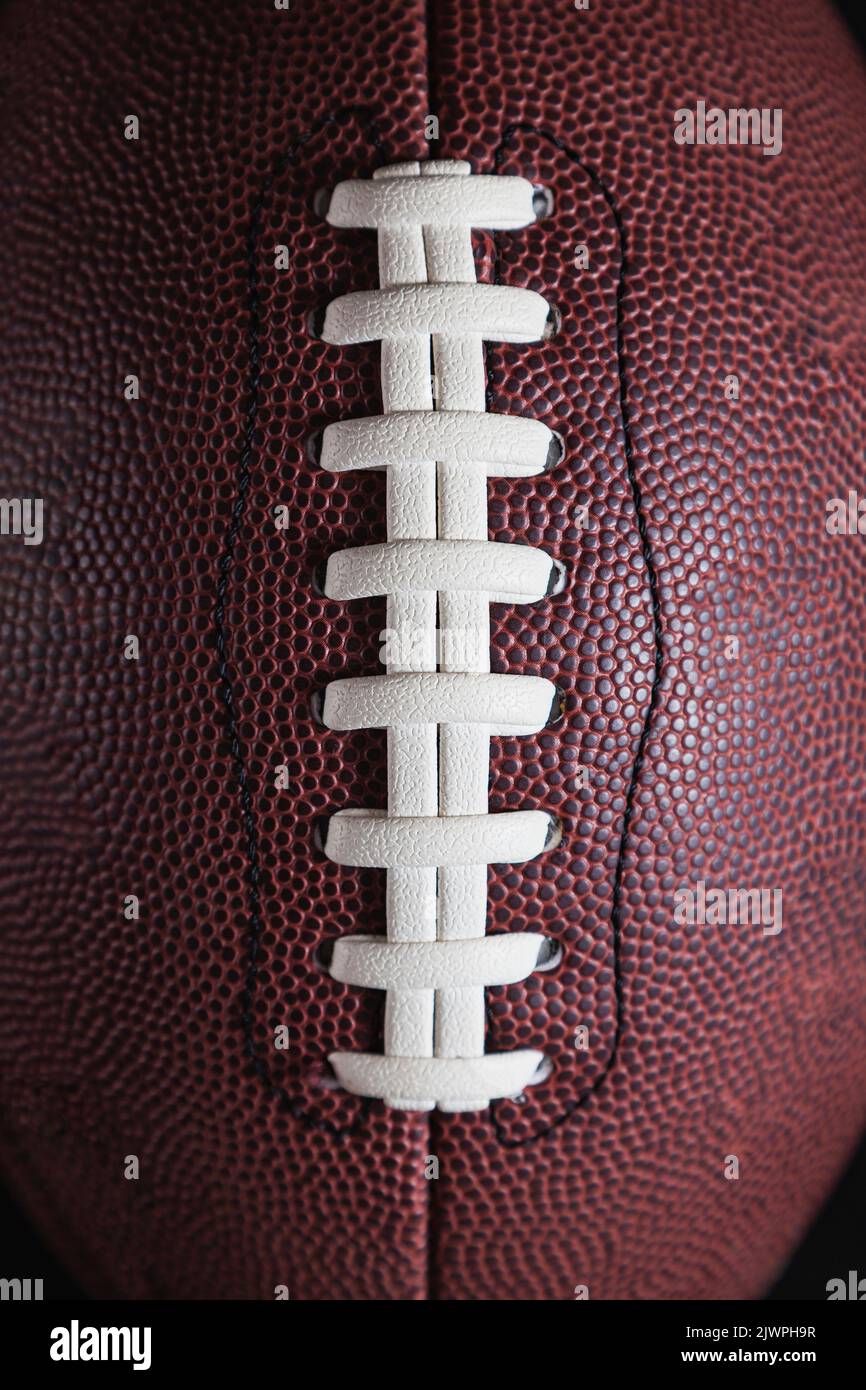 Dettaglio delle corde di una palla da calcio americana. Il pizzo è bianco e la palla è in composito marrone. Lo sfondo è nero. Foto Stock