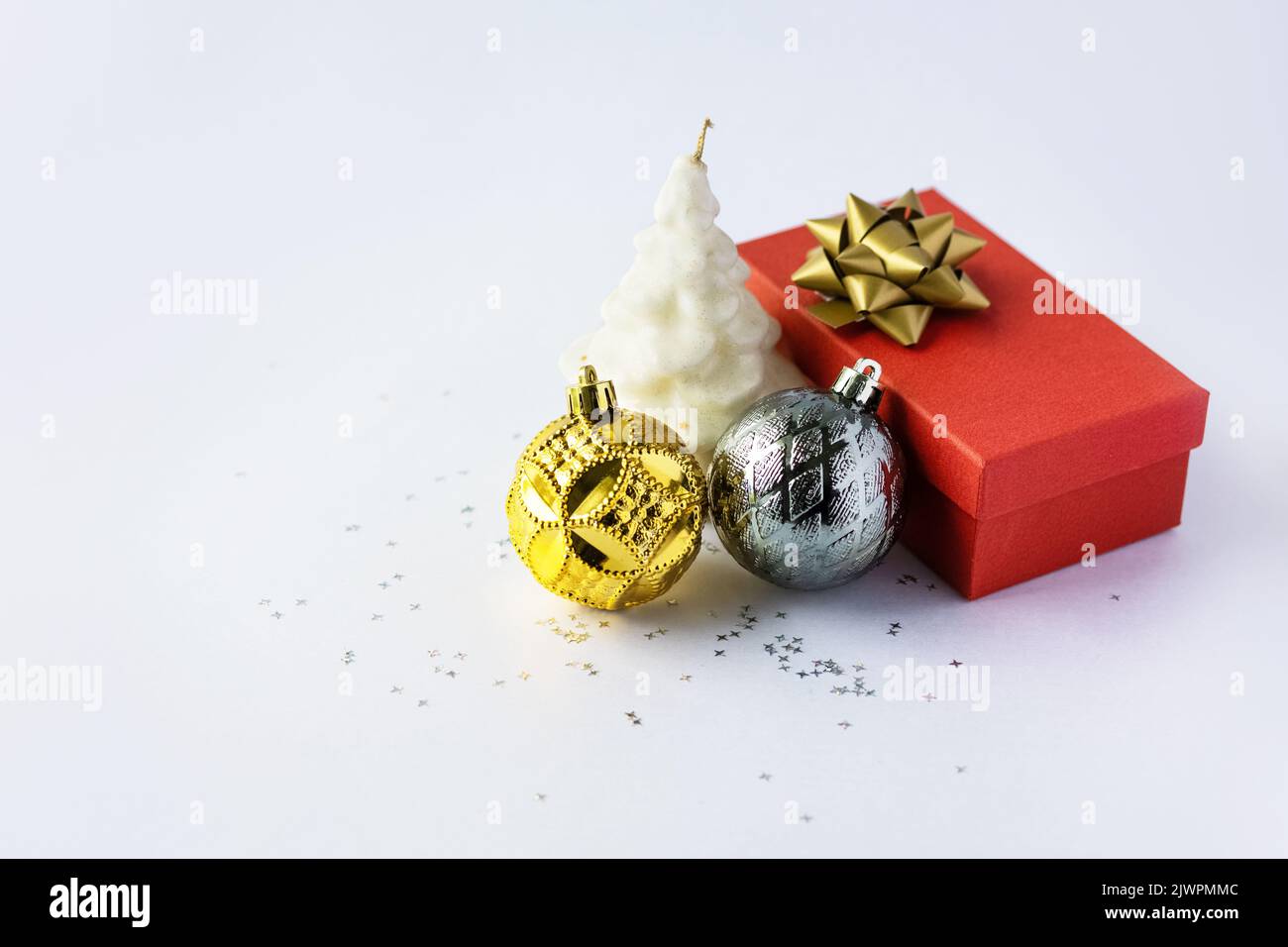 Natale composizione di una scatola regalo rossa con un arco d'oro, oro e argento palline di Natale e una candela bianco albero di Natale su uno sfondo grigio con Foto Stock