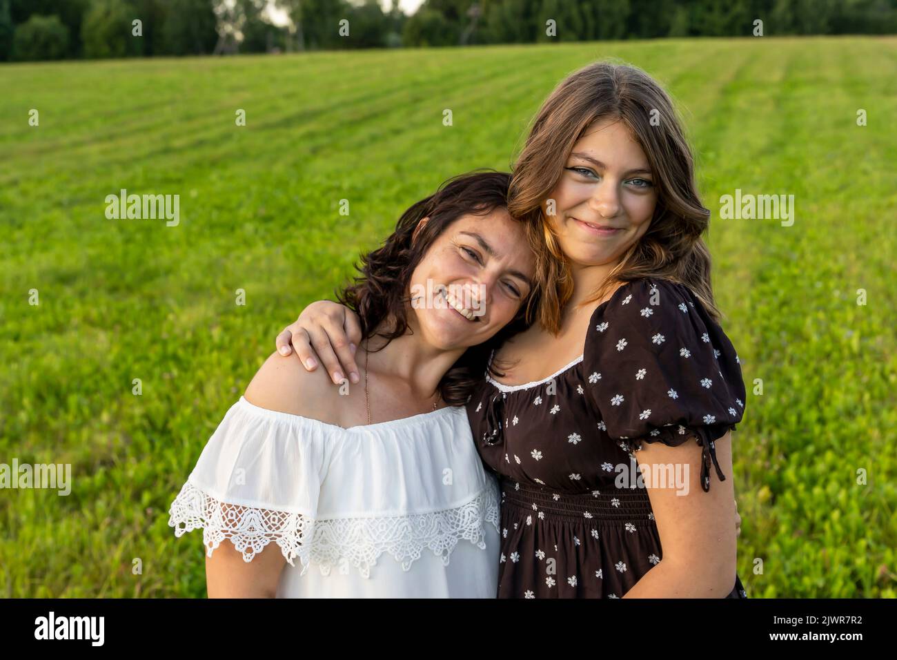 la mamma felice abbraccia la sua figlia adolescente contro un campo verde Foto Stock