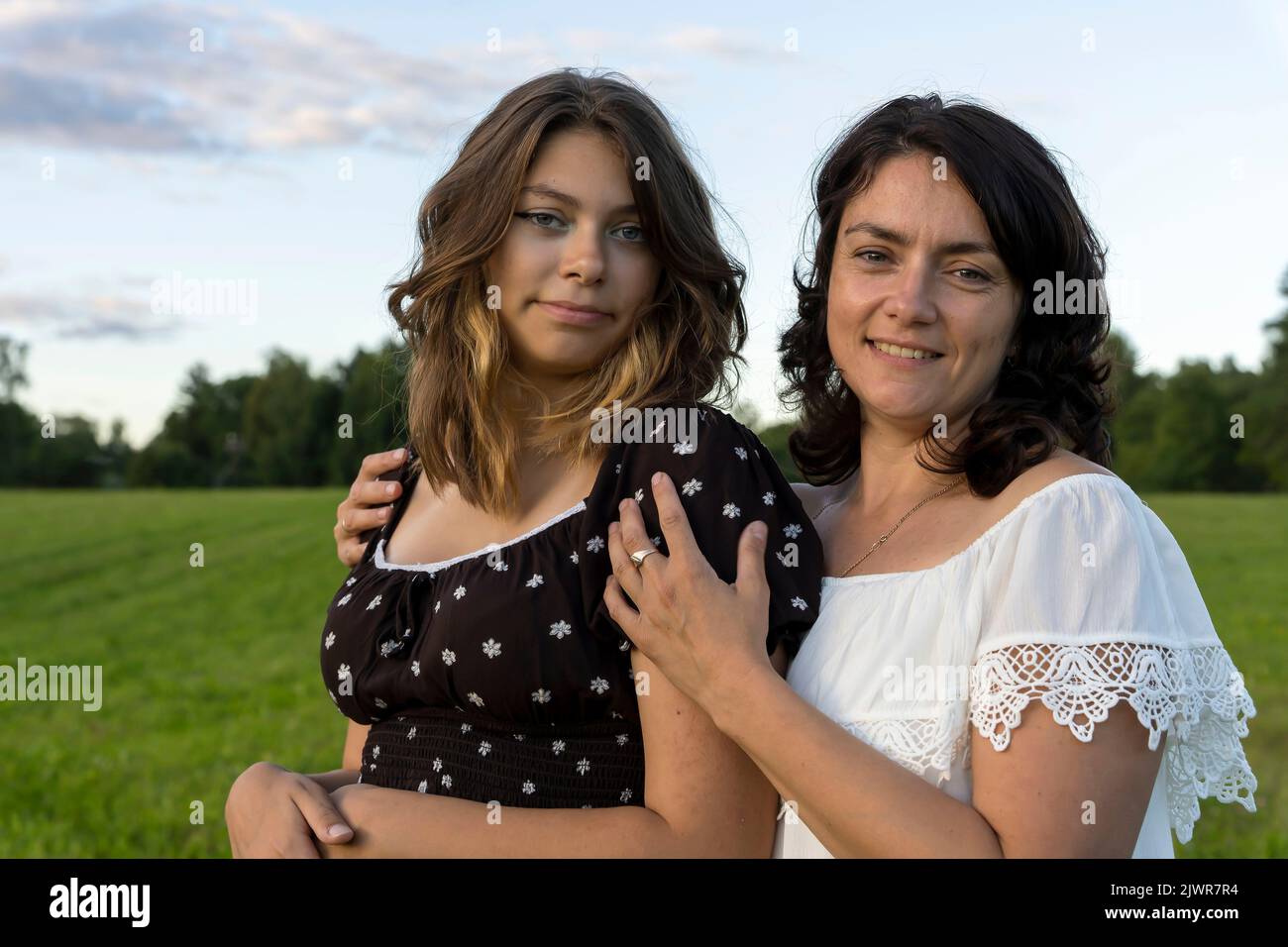 la mamma felice abbraccia la sua figlia adolescente contro un campo verde Foto Stock