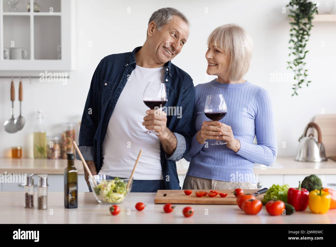 Sposi anziani che amano bere vino mentre cucinano insieme Foto Stock