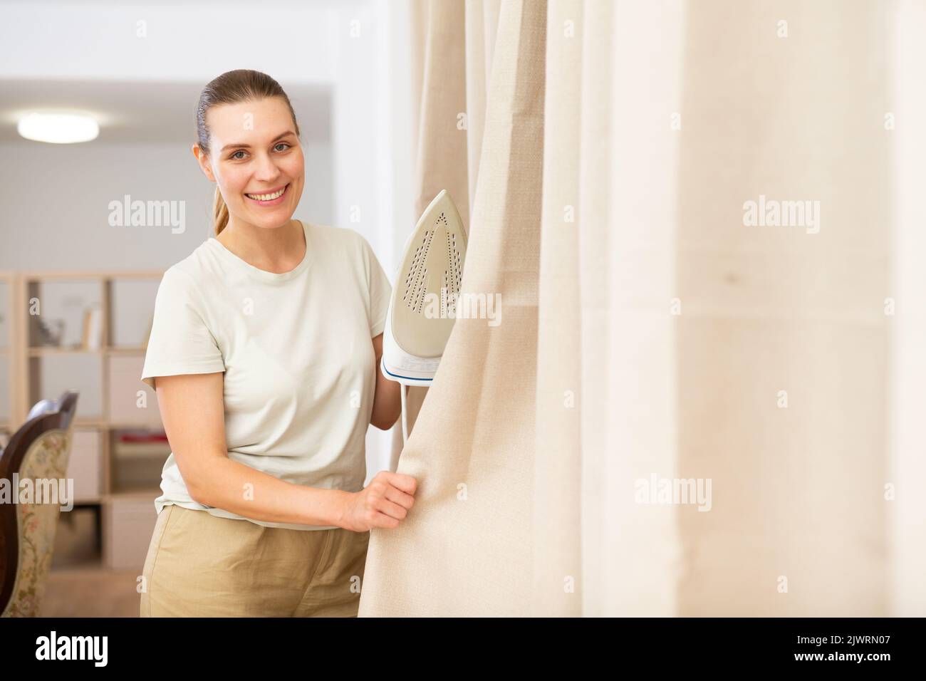 Giovane donna che stira le tende a casa Foto Stock