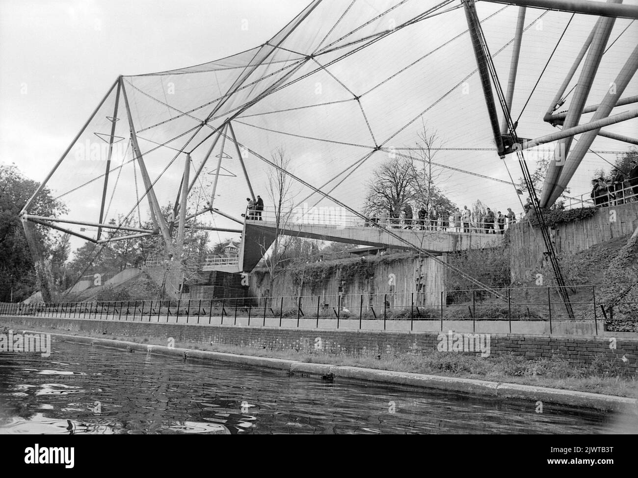 Londra, Inghilterra, circa 1967. Una vista sulla Snowdon Aviary dello Zoo di Londra dal Regent’s Canal. Costruito nel 1964, lo Snowdon Aviary è stato progettato da Frank Newby, Cedric Price, e Antony Armstrong-Jones, 1st conte di Snowdon. Era la prima voliera pubblica britannica. Il London Zoo (noto anche come London Zoological Gardens) è situato al confine settentrionale del Regent's Park, al confine tra la città di Westminster e il quartiere di Camden. È lo zoo scientifico più antico del mondo. Foto Stock