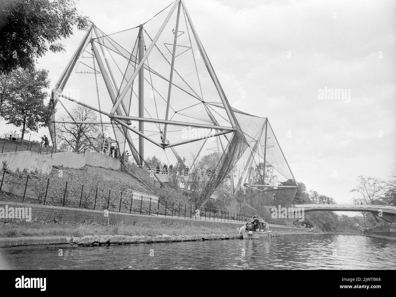 Londra, Inghilterra, circa 1967. Una vista sulla Snowdon Aviary dello Zoo di Londra dal Regent’s Canal. Una barca da diporto è ormeggiata a fianco e un ponte pedonale attraversa il canale in lontananza. Costruito nel 1964, lo Snowdon Aviary è stato progettato da Frank Newby, Cedric Price, e Antony Armstrong-Jones, 1st conte di Snowdon. Era la prima voliera pubblica britannica. Il London Zoo (noto anche come London Zoological Gardens) è situato al confine settentrionale del Regent's Park, al confine tra la città di Westminster e il quartiere di Camden. È lo zoo scientifico più antico del mondo. Foto Stock