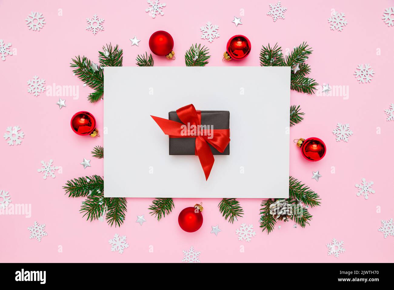 Natale, Capodanno disposizione vacanza. Scatola regalo nera con arco rosso in cornice di rami di abete naturale e decorazioni su fondo piatto bianco e rosa pastello Foto Stock