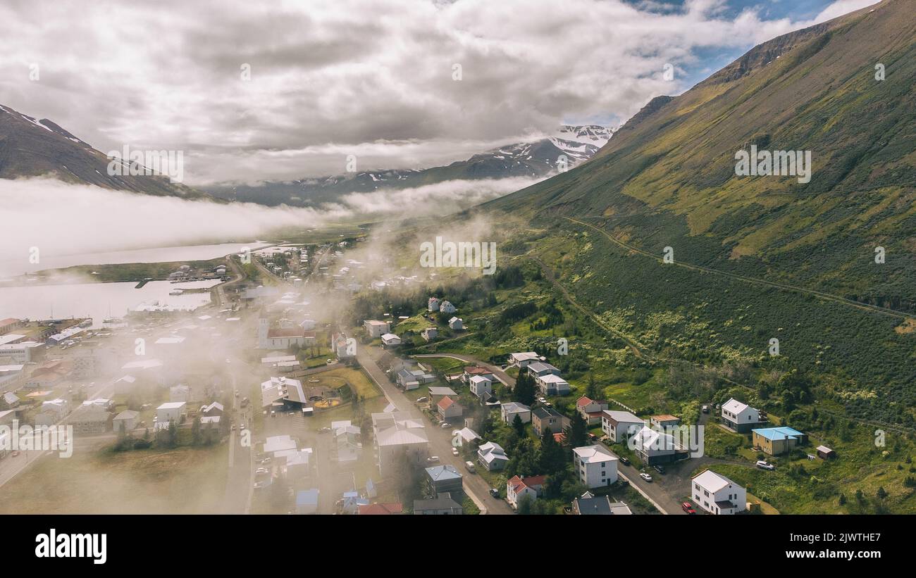 Nebbia mattutina sopra la piccola città nel mezzo delle montagne dell'Islanda settentrionale - Siglufjordur Foto Stock
