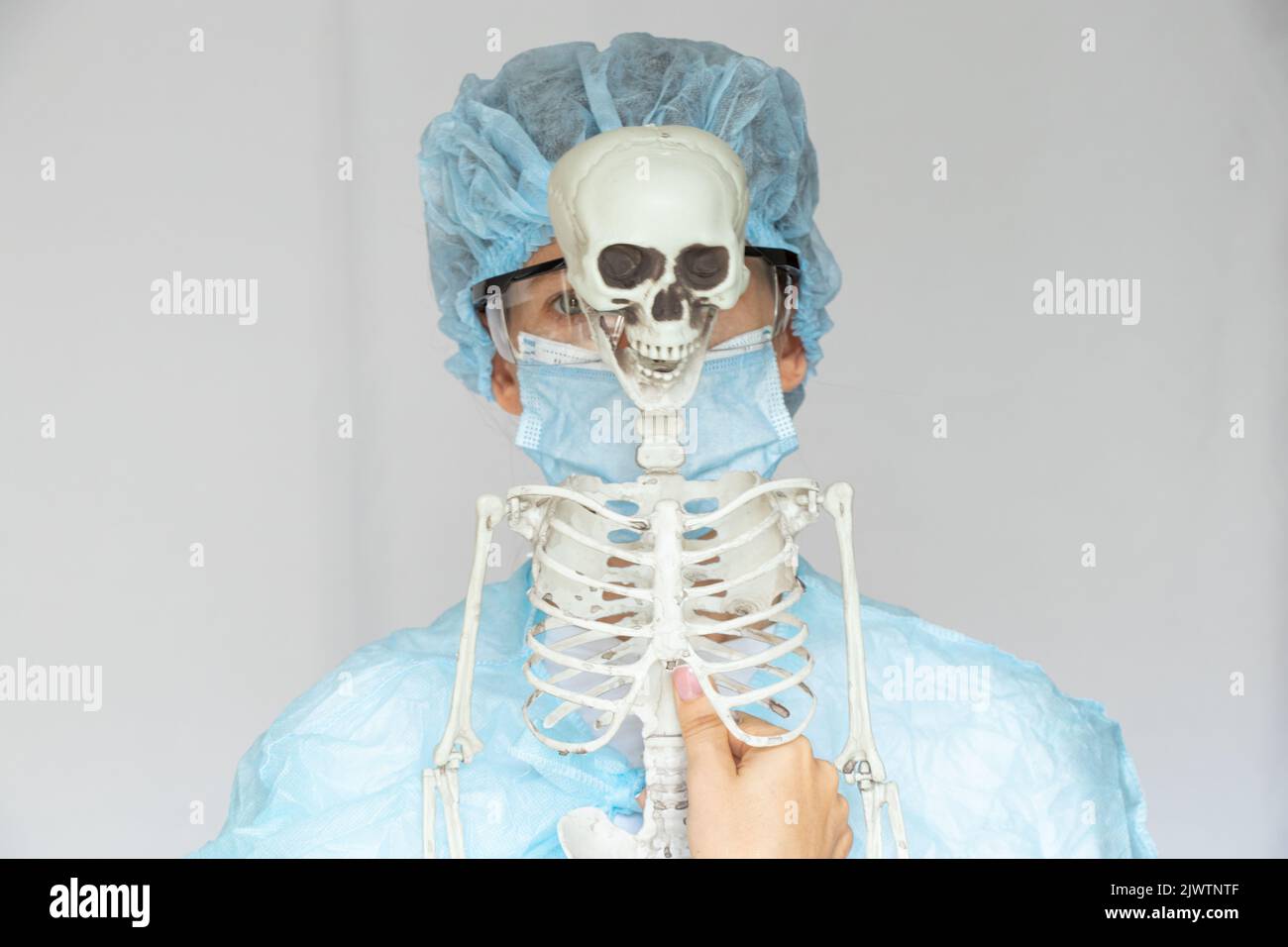 Ragazza medico in un cappotto con occhiali e una maschera e uno scheletro su uno sfondo isolato, un medico in un vestito medico, medicina Foto Stock