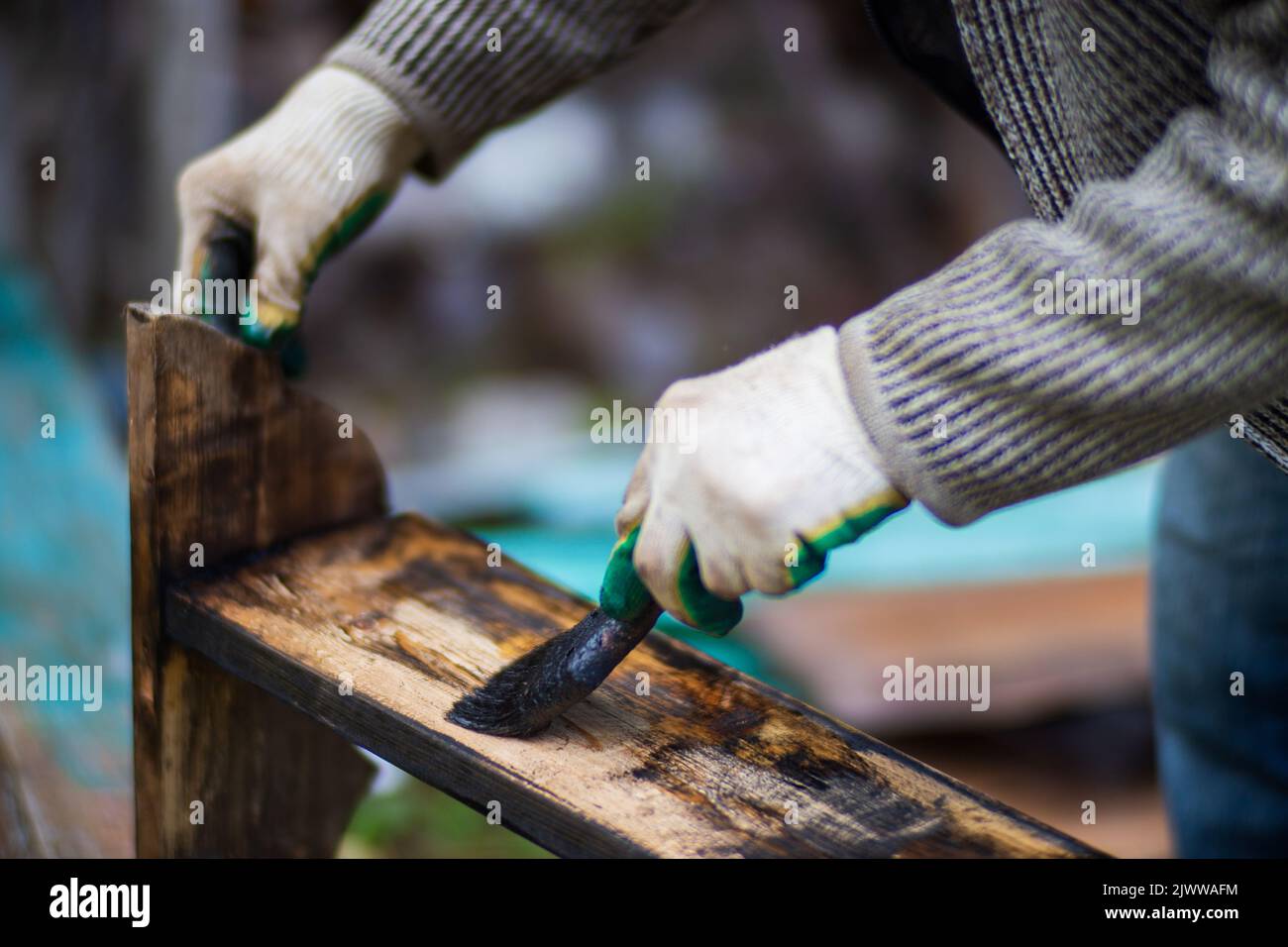 Un uomo applica la vernice su una superficie di legno con un pennello. Lacca Foto Stock