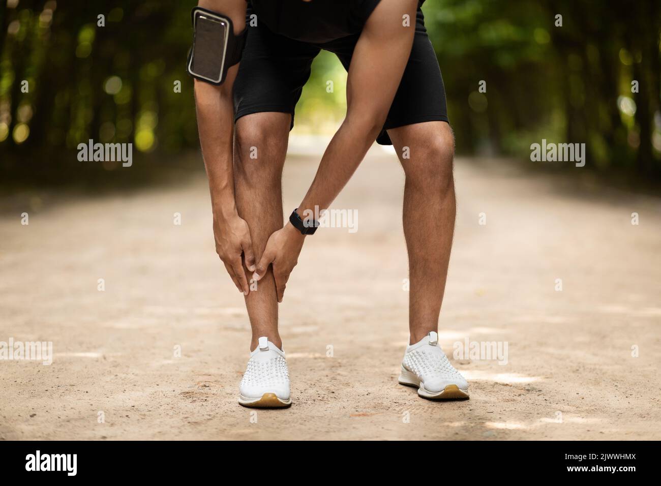 Corto di sportivo nero che si esercita nel parco pubblico, toccando la caviglia Foto Stock