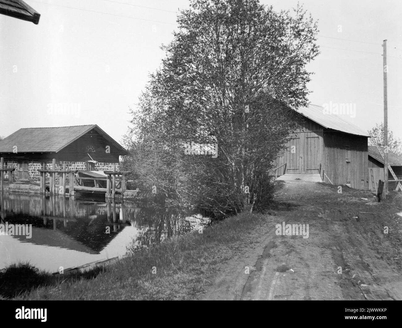 Il mulino di Åsmundshyttan, il tronco di trebbiatura e le dighe. Fotografato dall'ingresso sulla strada di campagna ad est del fiume. Åsmundshyttans kvarn, trösklogen och dammanläggningen. Fotografad från infarten vid landsvägen öster om ån. Foto Stock