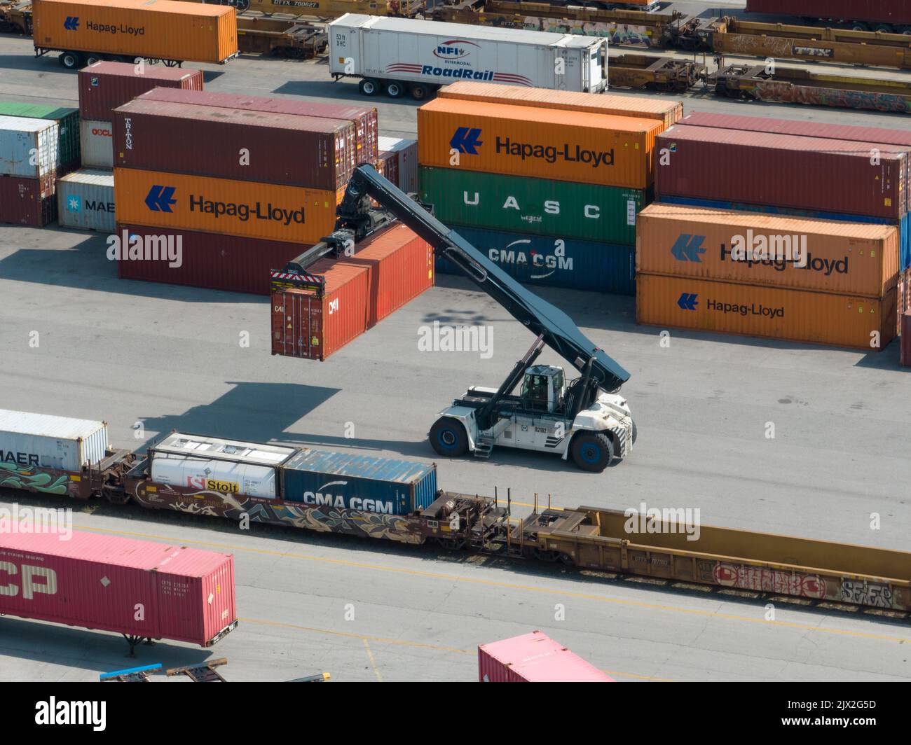 Una foto aerea di un contenitore di spedizione che viene spostato da un carrello industriale di grandi dimensioni in un terminale di spedizione. Foto Stock