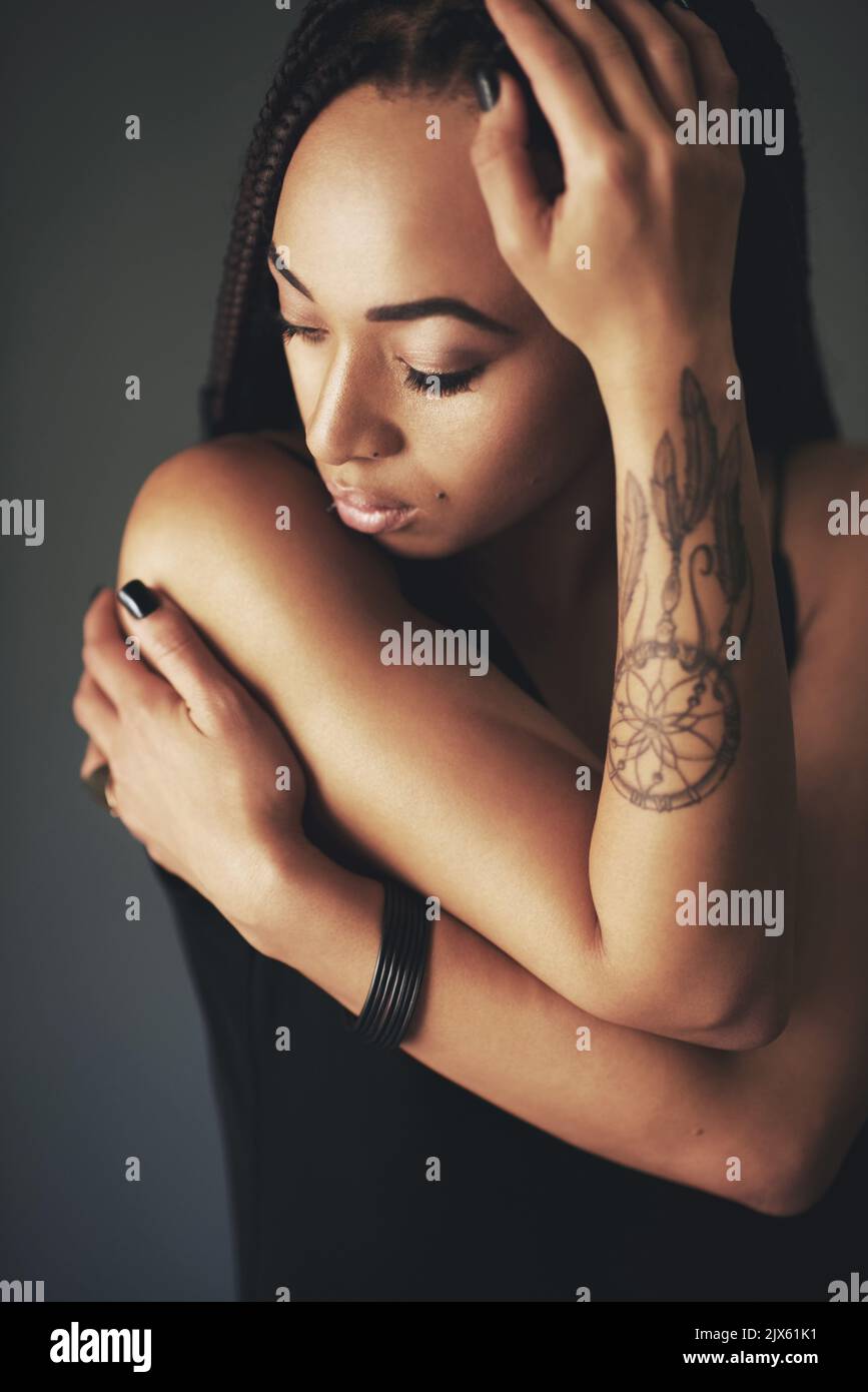 Indossa le sue emozioni sulla manica. Studio shot di una bella giovane donna con un tatuaggio sul braccio su uno sfondo grigio. Foto Stock