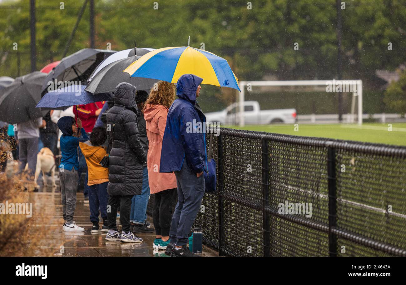 Vista posteriore di persone con ombrelloni in piedi sotto la pioggia allo stadio di calcio waching. Pioggia intensa, persone sotto gli ombrelloni. Foto di viaggio, vista strada- Foto Stock
