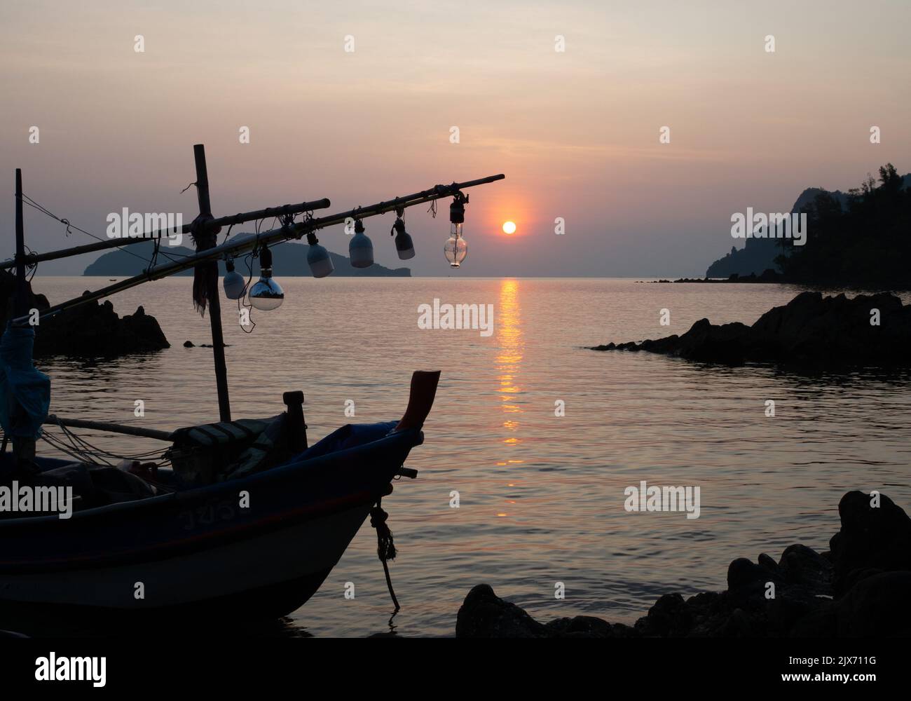 una barca da pesca ferma sulla costa al tramonto Foto Stock