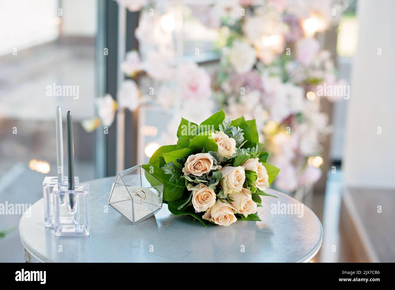 Un paio di splendidi anelli da sposa in un moderno piedistallo di vetro e un delicato bouquet di rose da sposa. Matrimonio, cerimonia. Messa a fuoco selettiva morbida. Foto Stock