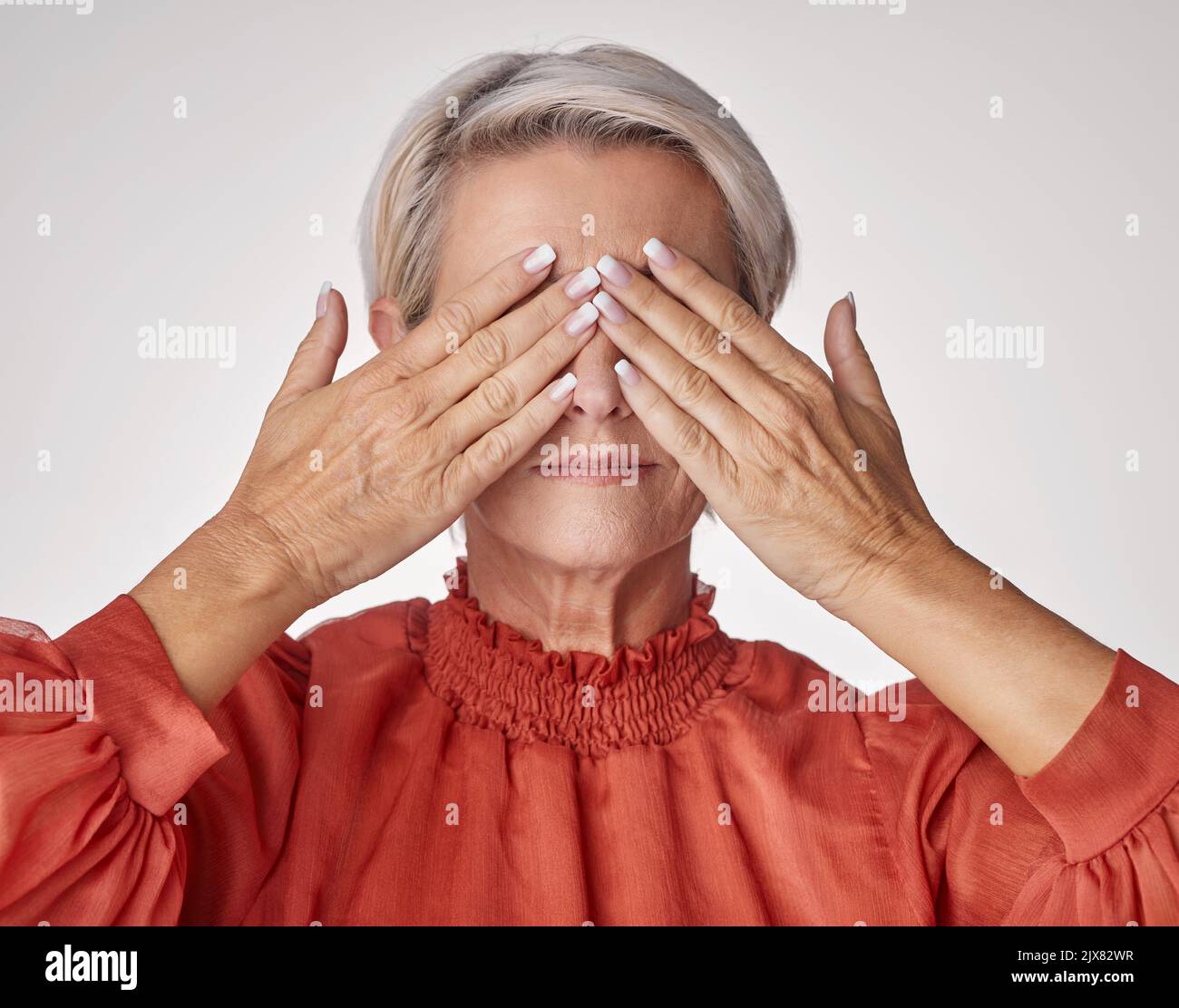 Senior, mani e coprendo gli occhi o il volto di una donna matura che soffre di mal di testa o sforzo oculare mentre si posa su uno sfondo grigio studio. Anziani Foto Stock