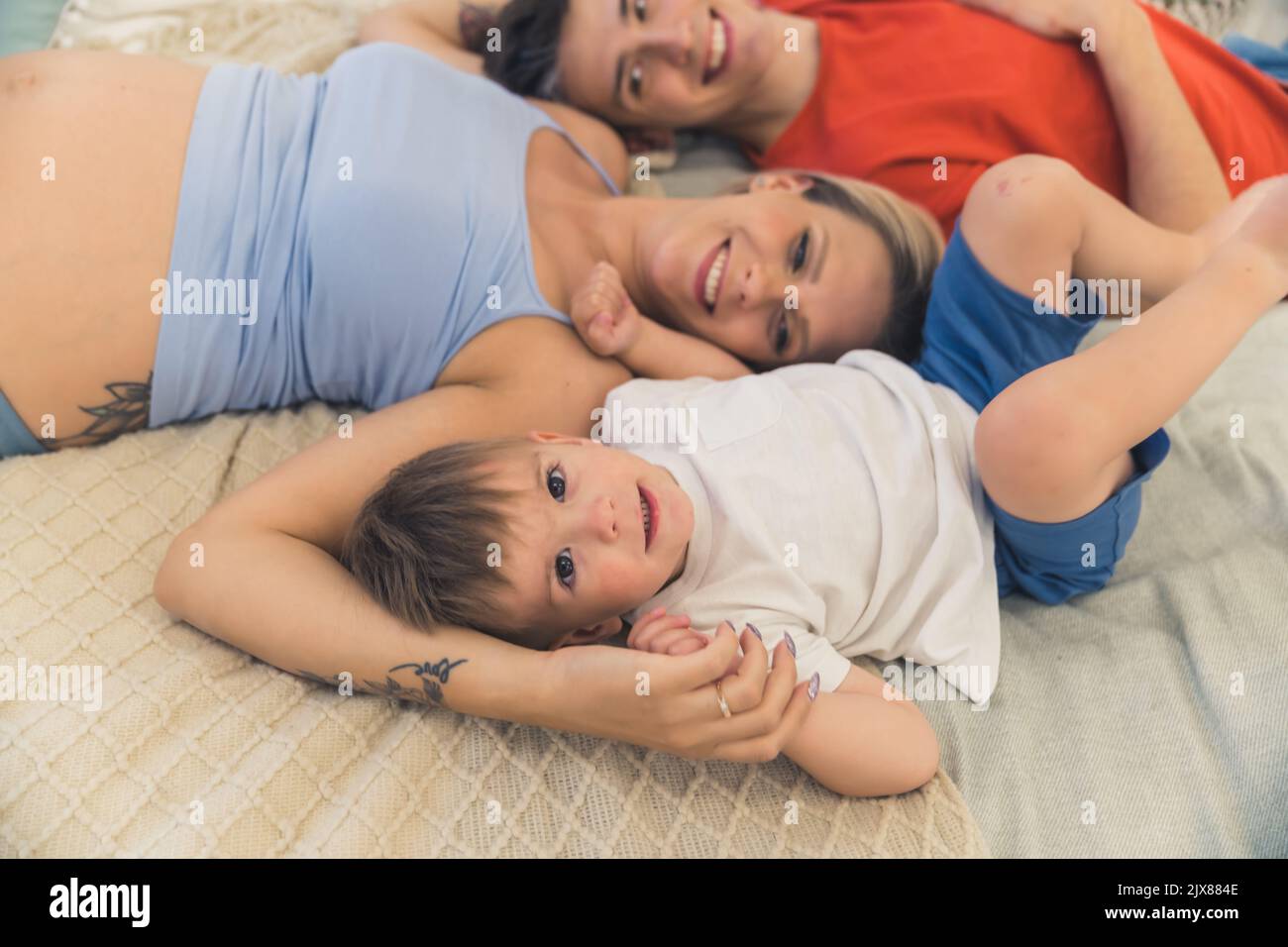 Relazioni familiari sane. Coppia eterosessuale caucasica sposata sdraiata sul letto con il figlio di quattro anni e solletico l'un l'altro. Foto di alta qualità Foto Stock
