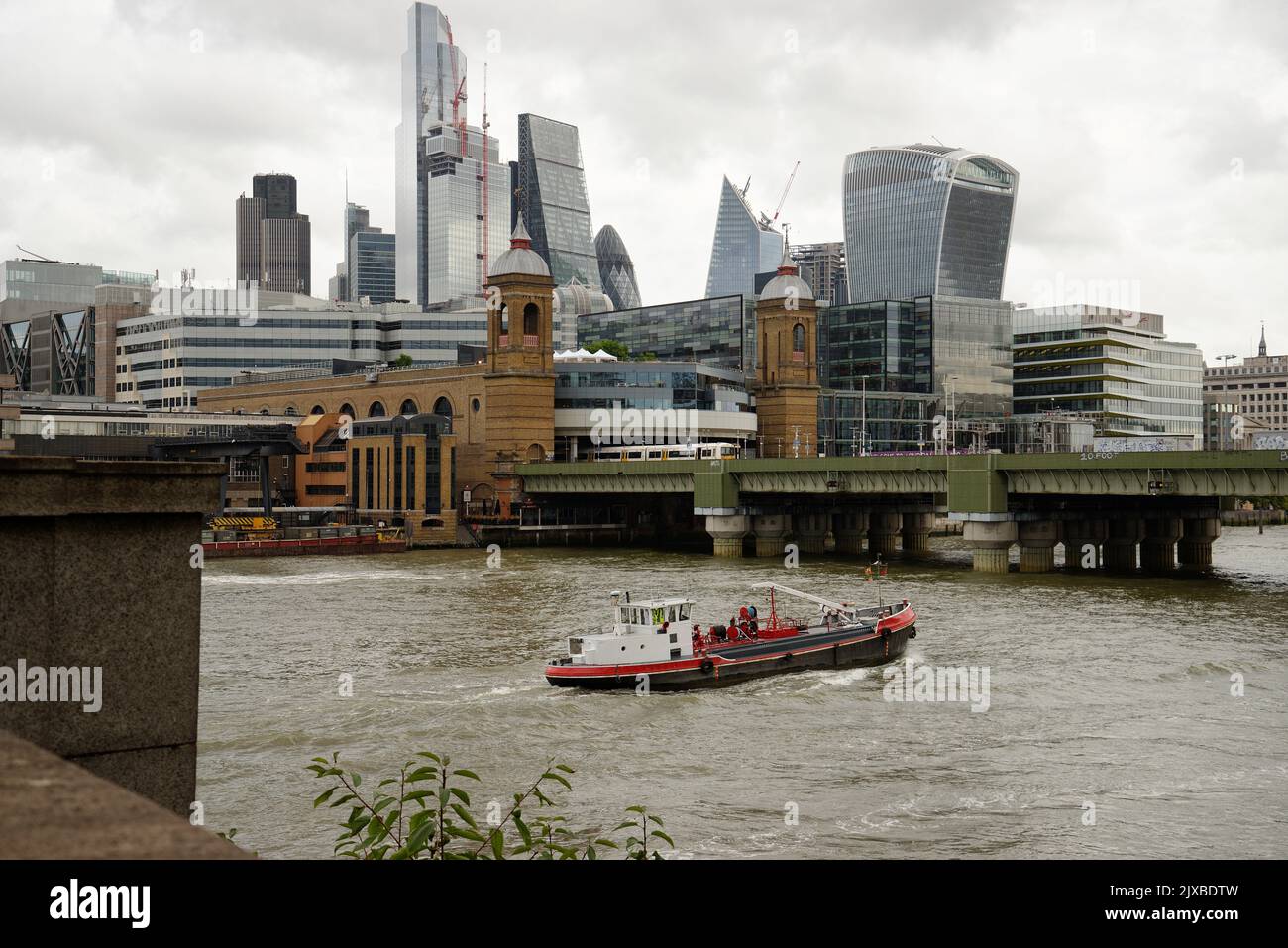 La città di Londra da Southwark Bridge con una barca chiamata Helena con una gru sul suo ponte. Foto Stock