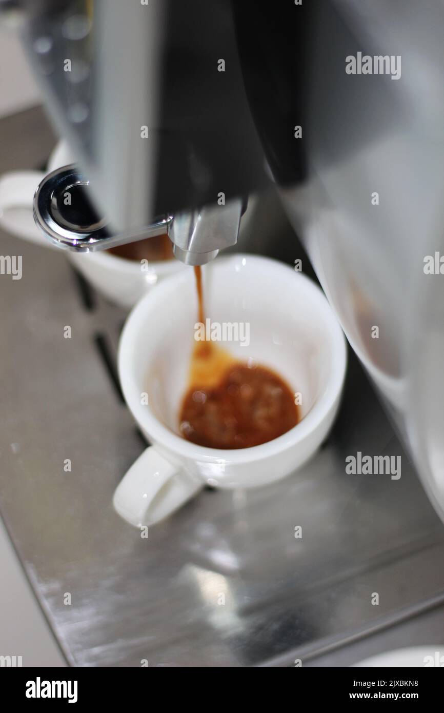 Espresso aromatico gocciolante in due tazze bianche. Macchina per caffè espresso. Foto Stock