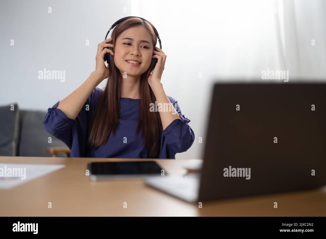 Sorridente ragazza che si rilassa a casa, sta suonando musica utilizzando un computer portatile e indossando cuffie Foto Stock