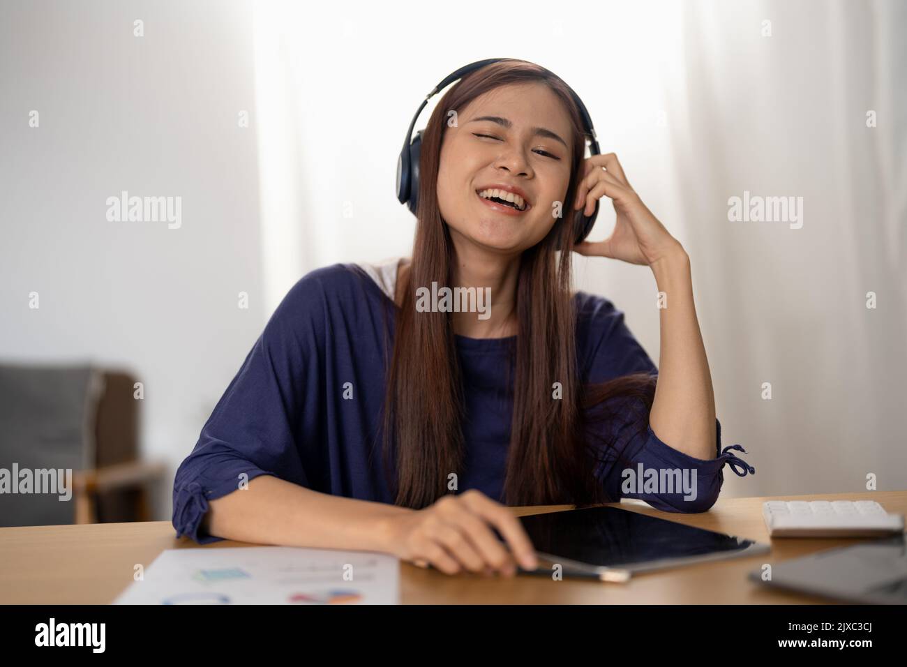 Sorridente ragazza che si rilassa a casa, sta suonando musica utilizzando un tablet digitale e indossando cuffie bianche Foto Stock