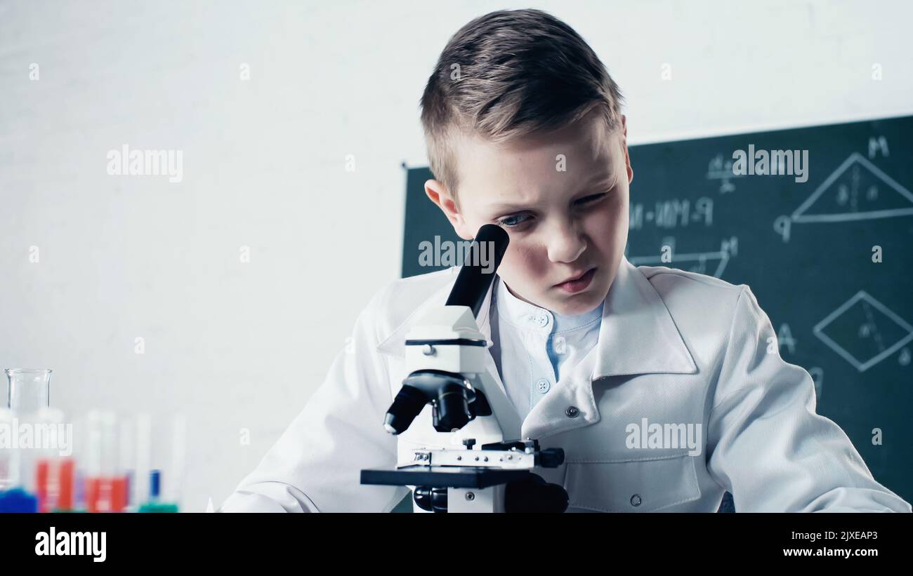scolaro in cappotto bianco che guarda attraverso il microscopio durante la lezione di chimica in classe, immagine stock Foto Stock