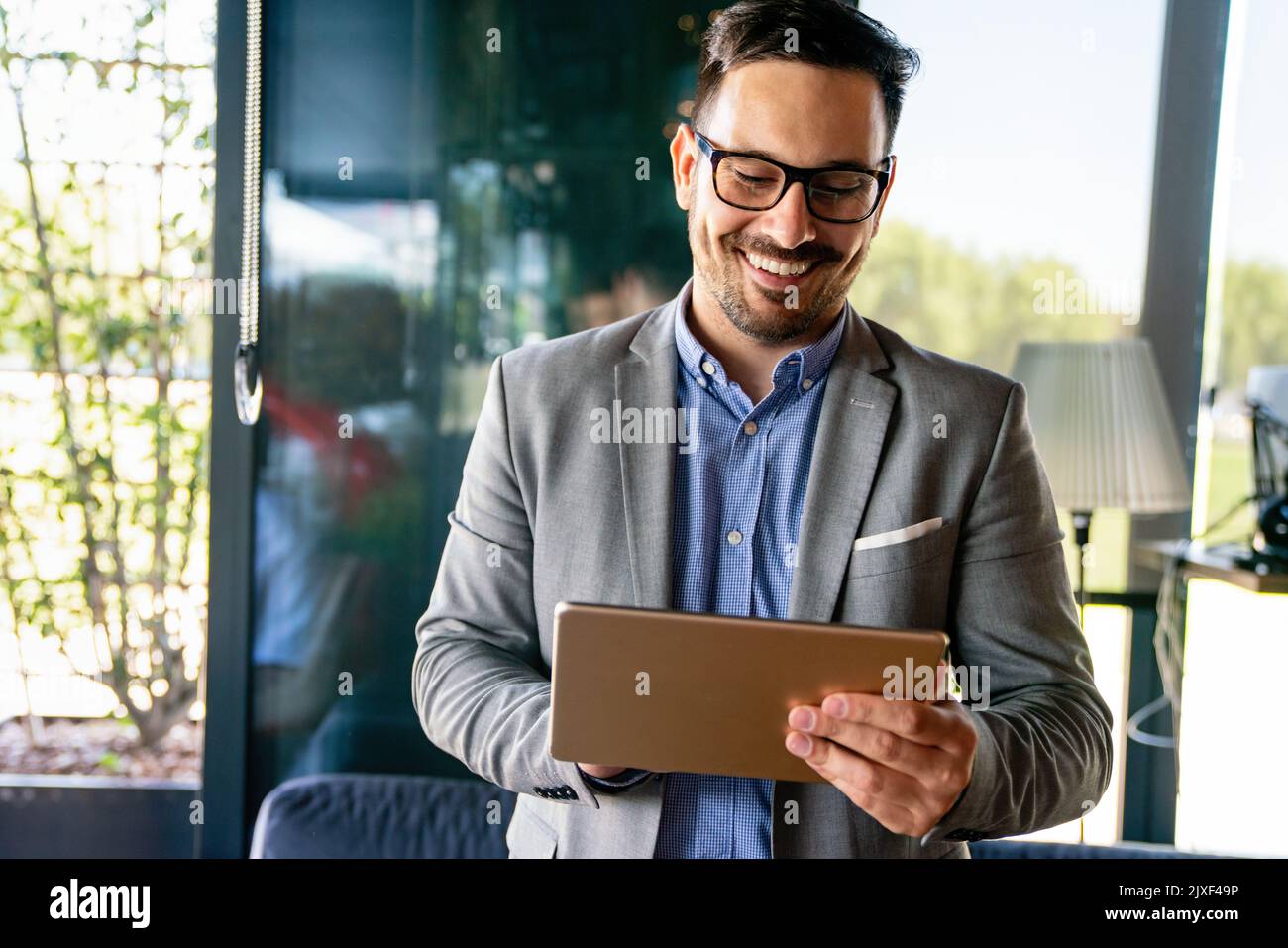 Giovane uomo d'affari sorridente di successo, imprenditore in una suite aziendale formale che lavora su tablet Foto Stock