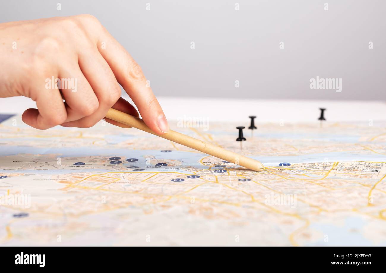 La mano punta con la matita verso la posizione sulla mappa con i puntini. Pianificazione dell'itinerario di viaggio. Donna che pensa viaggio percorso sopra o mostrarlo. Viaggio, navigazione c Foto Stock