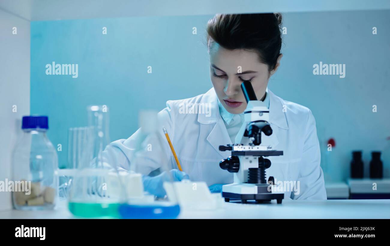 allettante per gli scienziati che scrivono i risultati dell'analisi vicino al microscopio in laboratorio clinico, immagine di scorta Foto Stock