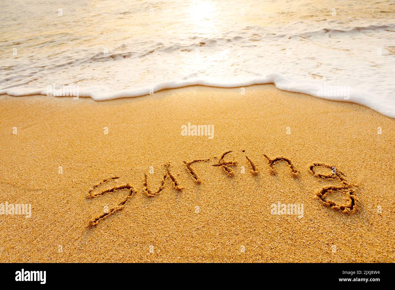 La parola Surfing scritto nella sabbia sulla spiaggia Foto Stock