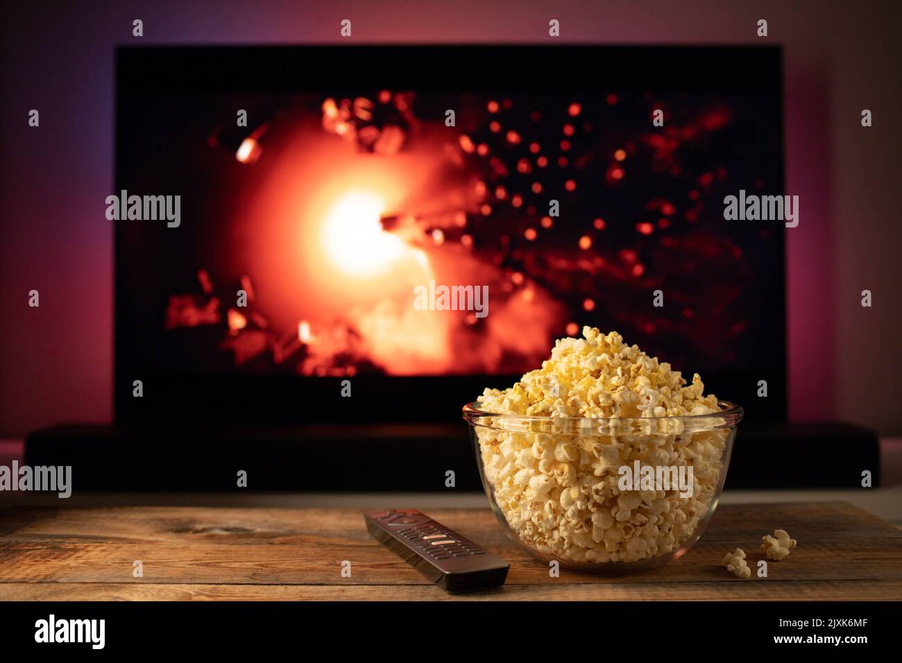 Una ciotola di vetro di popcorn e il telecomando in background il televisore funziona. Serata accogliente guardando un film o una serie TV a casa Foto Stock