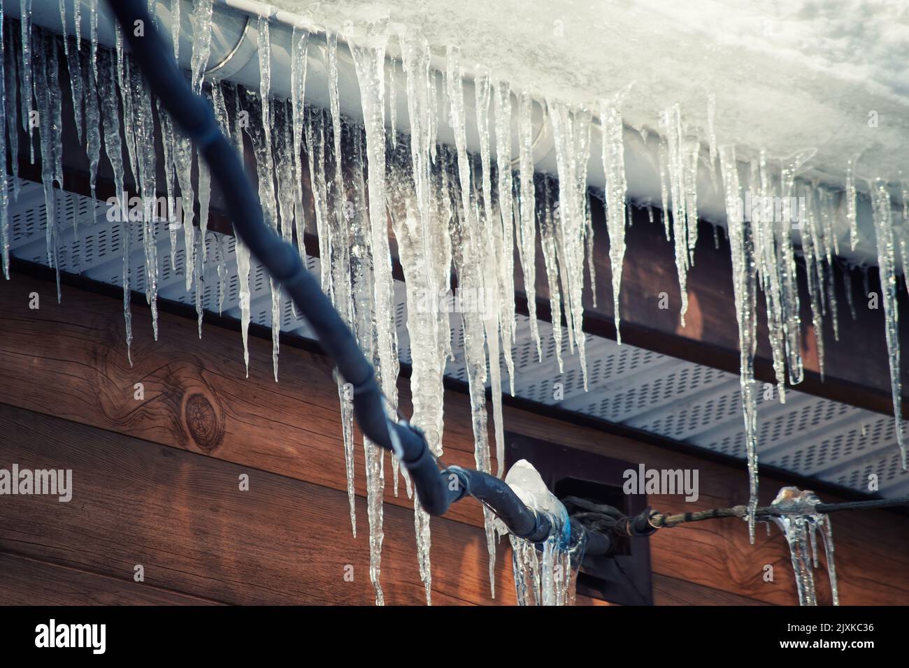 Ghiaccioli pericolosi sui cavi elettrici sotto il tetto della casa. Specifico per la stagione invernale Foto Stock