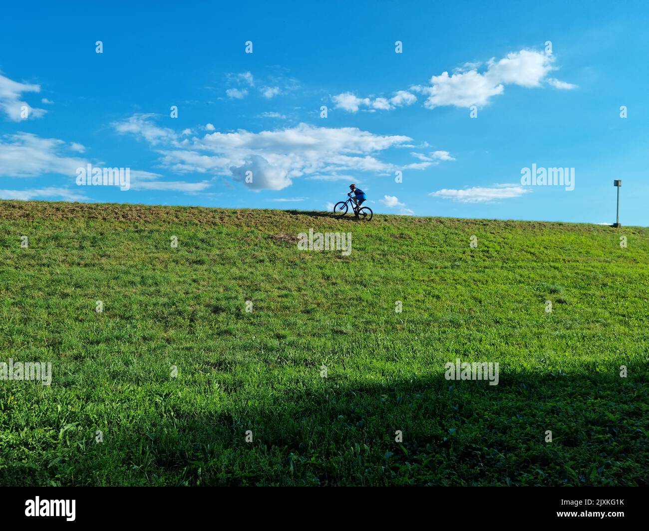 Un tiro a basso angolo di una persona in bicicletta su una collina verde sotto un cielo blu Foto Stock