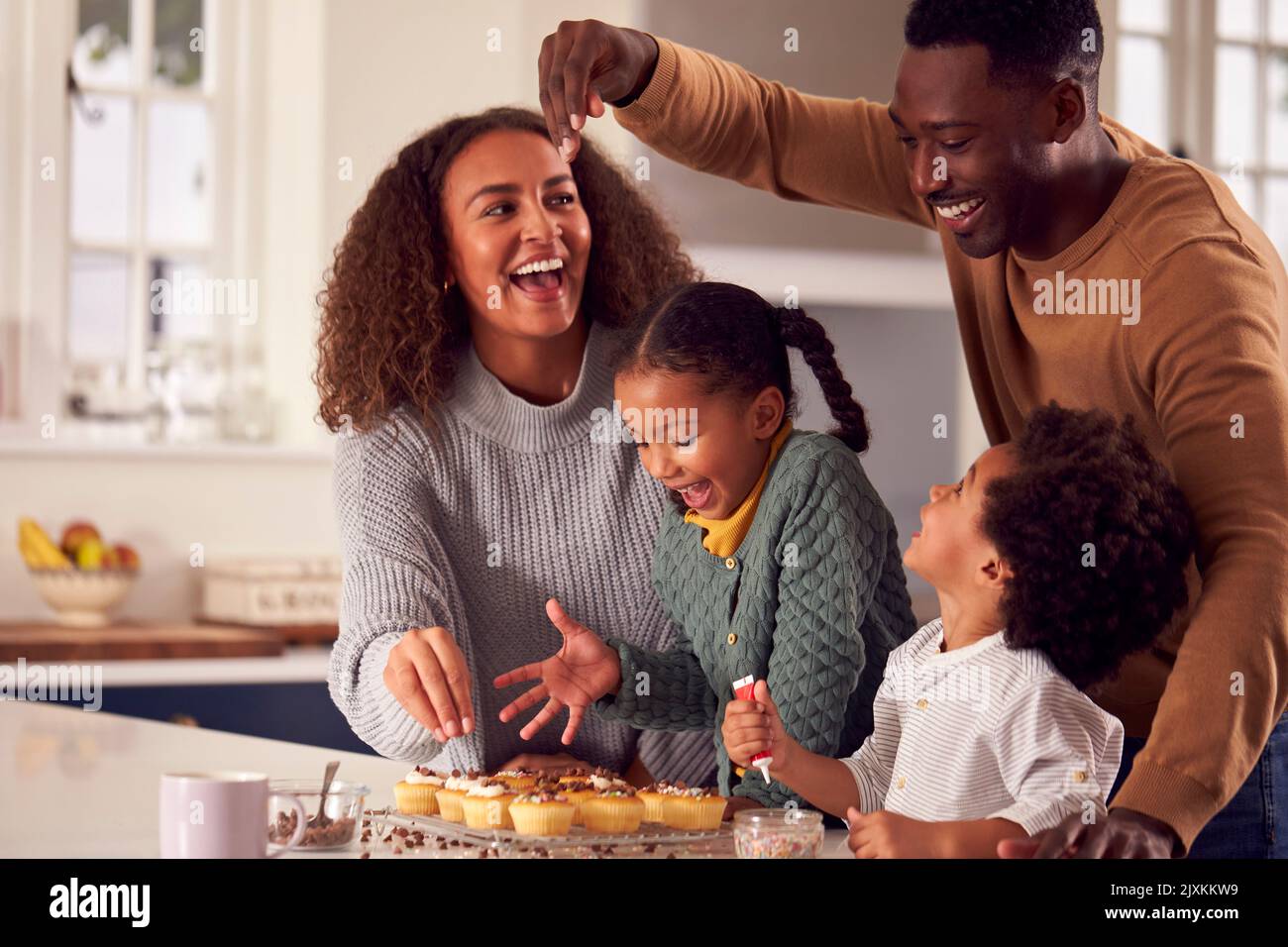 Famiglia cottura Cupcakes seduti intorno al bancone della cucina a casa Foto Stock