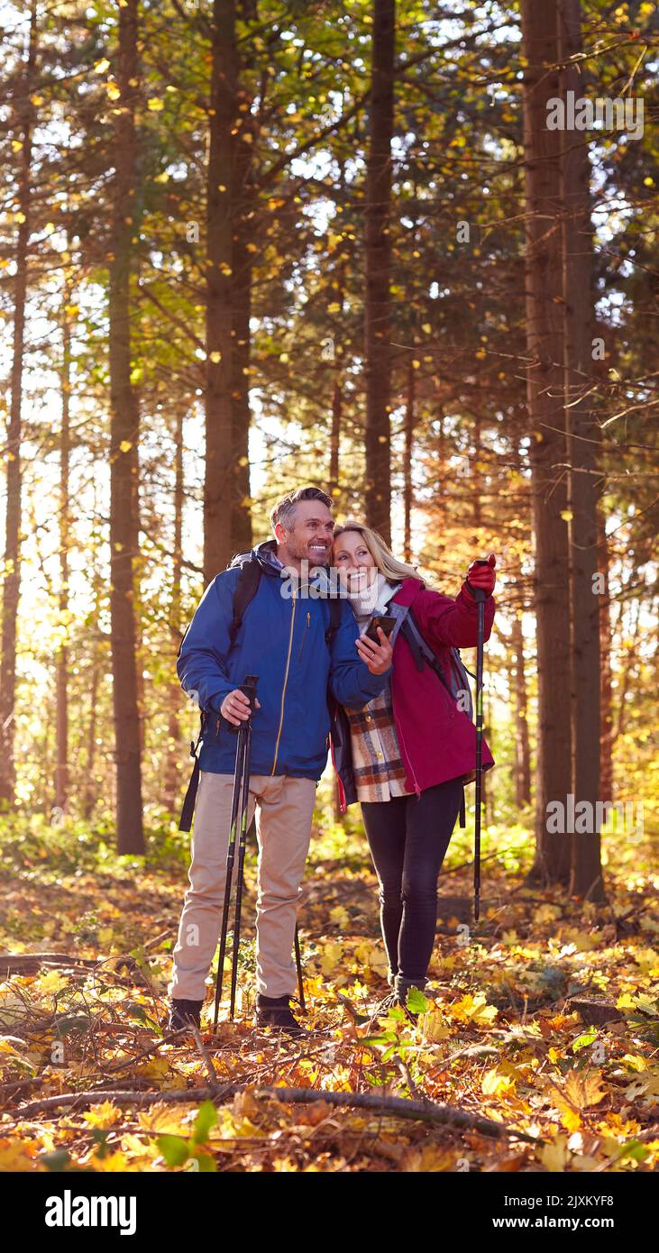 Una coppia matura in pensione cammina in autunno o in inverno nella campagna utilizzando la mappa o l'app di navigazione sul telefono cellulare Foto Stock